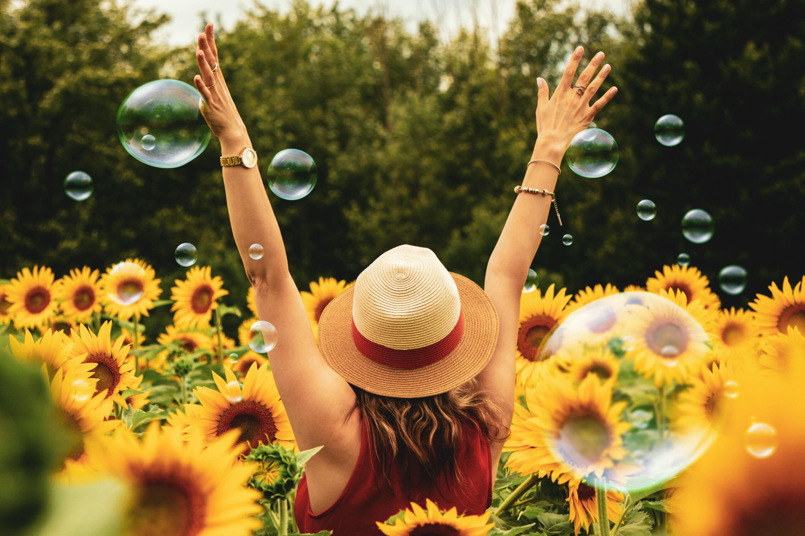 our-story A joyful woman in a sunflower field with bubbles, expressing happiness on a summer day.